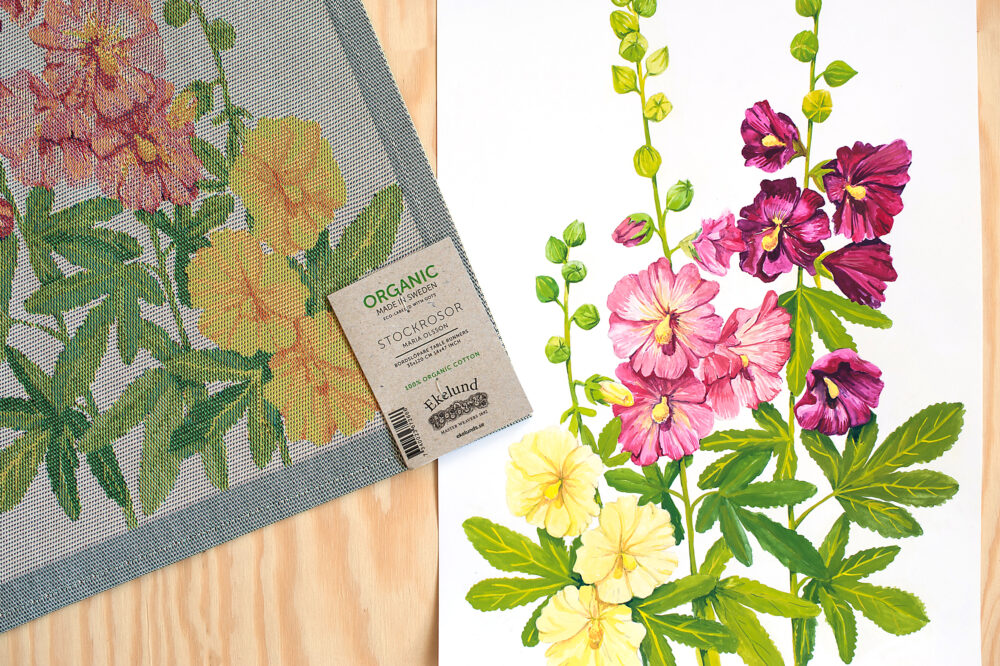 Bilden föreställer en vävd handduk och en illustration av blomman stockros i gult, rosa och mörkviolett.