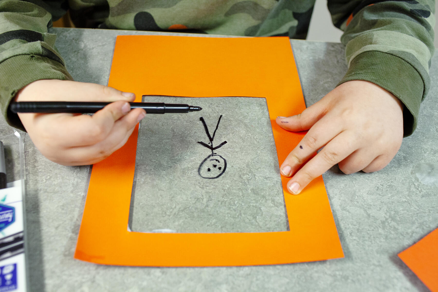 Barnhänder som målar en streckgubbe inom en orange passepartout.
