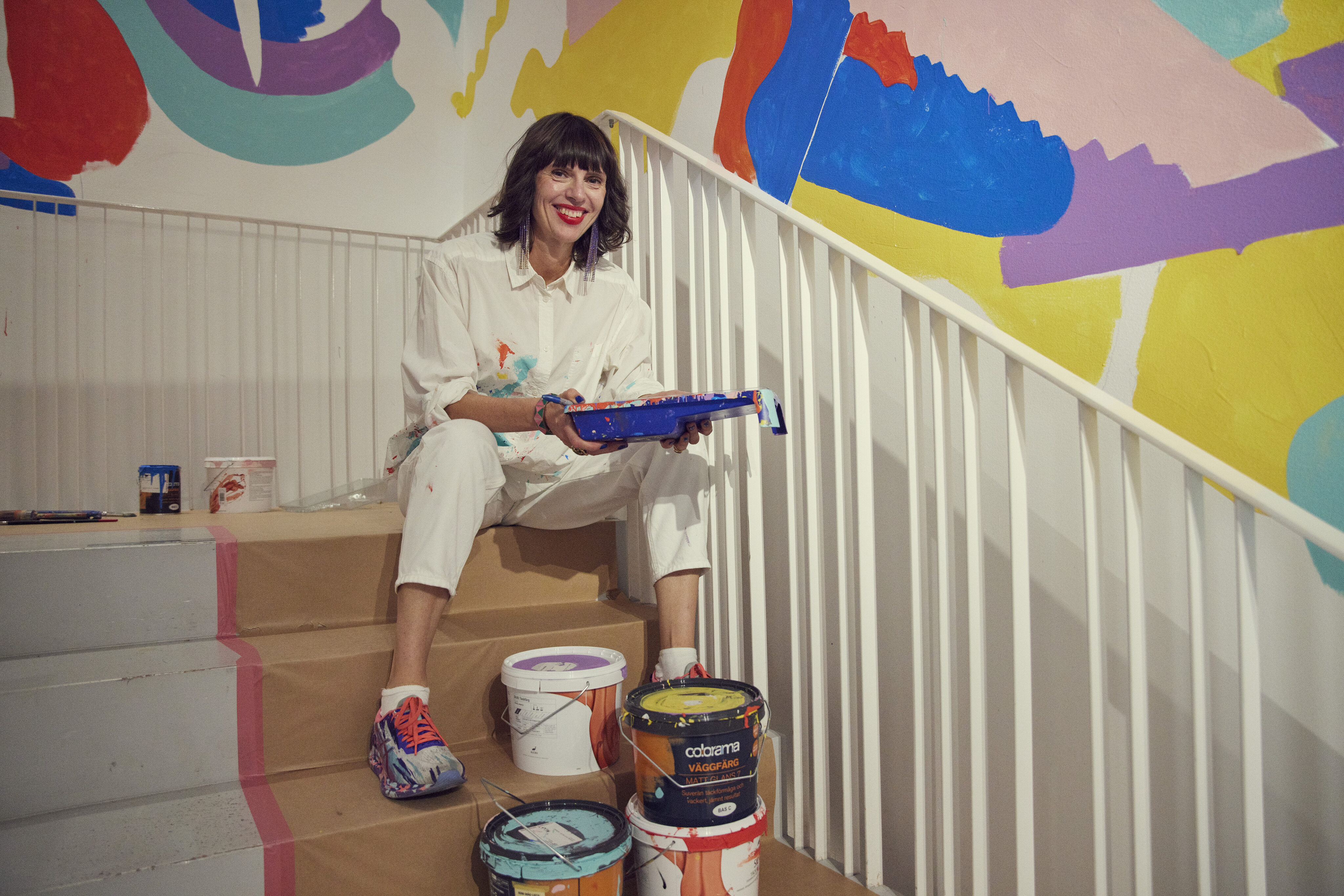 Kvinna sitter i trappa med målarfärger runt sig