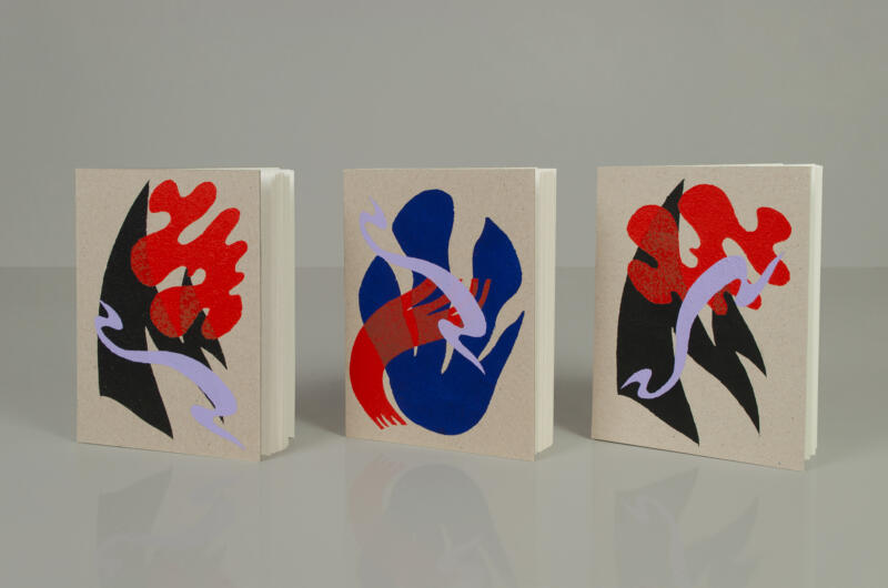 Tre handbunda och handtryckta skissböcker står på en blankgrå yta. Abstrakta motiv på omslagen i rött, svart, blått och syrenlila.