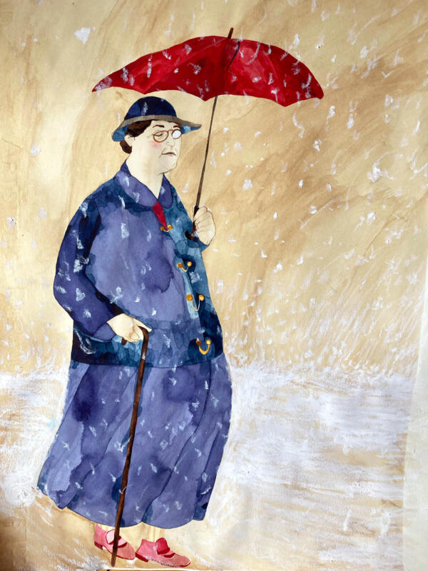 En färgbild av en dam med käpp som står under ett paraply och blundar medan det snöar