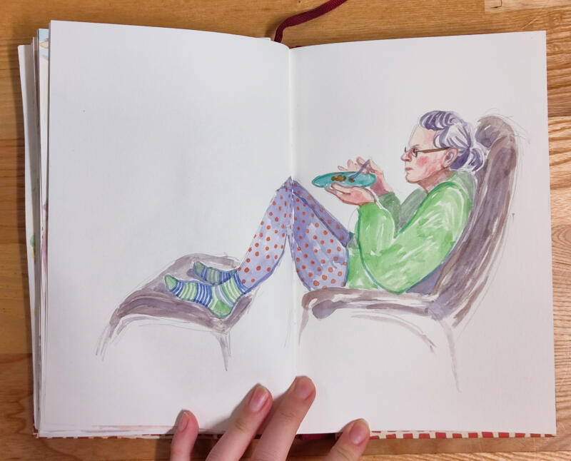 Akvarellmålning av en äldre kvinna som sitter bekvämt i en fåtölj med fötterna på en fotpall och äter chokladkaka. Hon har grått, halvlångt hår i en hästsvans, grön tröja, prickiga byxor och randiga strumpor.