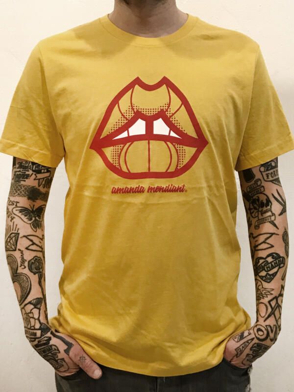 Beskuren bild på en man med tatueringar som bär en gul t-shirt med en röd mun.