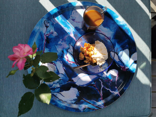 Akvarellmotiv tryckt på en bricka med fika uppdukad. En ros och en kopp kaffe,  solen strilar in. Design och foto Maria Helgars.