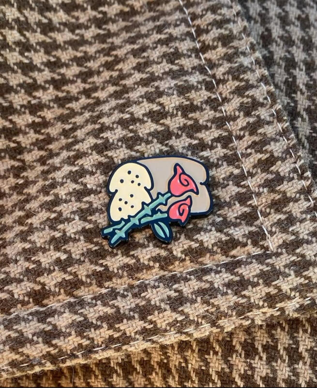 Emaljerad pin föreställandes bröd och rosor sitter på ett kavajslag