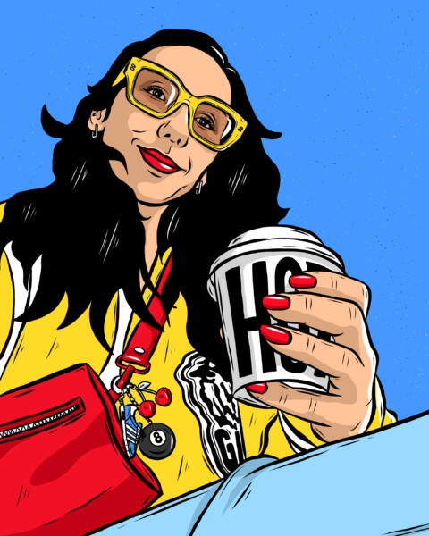 En tjej/kvinna som sitter med en kaffemugg i handen som det står "Hot" på. Hon har solglasögon på sig och ser lite glad ut. 