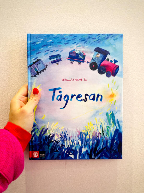 Bokomslag i akvarell och kollage till bilderboken ”Tågresan” för barn 3–6 år. Illustrationen föreställer ett tåg som färdas genom havets djup, omgiven av fiskar och växter. Omslaget kombinerar fantasi, lekfullhet och visuellt rik illustration för att locka målgruppen och förstärka berättelsens magiska och äventyrliga tema.