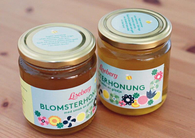 Två honungsburkar från Liseberg med en blommig etikett med lekfulla former och färg, samt ett bi som flyger.