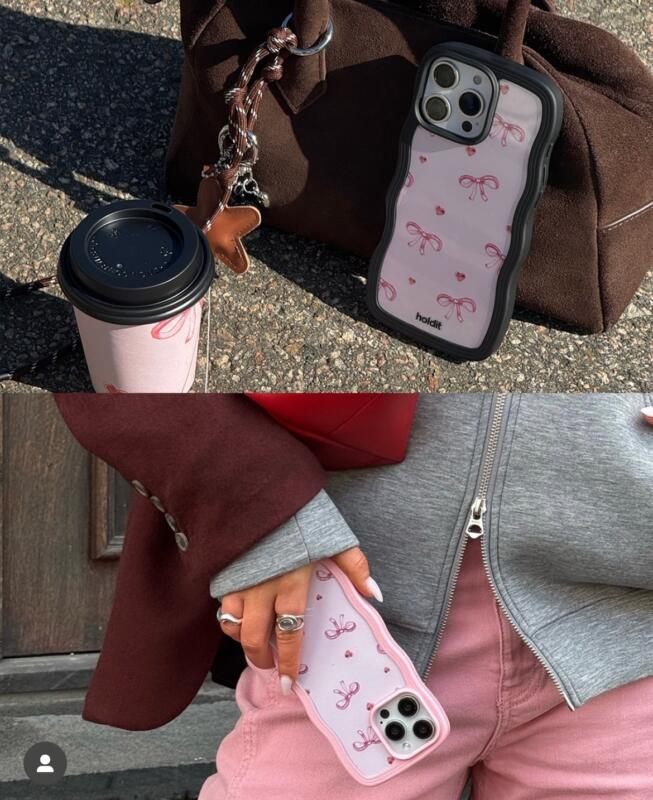 Rosa mobilskal med rosetter vid en väska, samt hållandes av en hand.