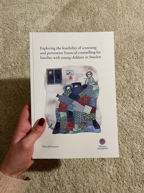 En bok som är en doktorsavhandling med illustrerad framsida av en kvinna som syr ett lapptäcke som två barn sover under. I bilden syns även en katt, strumpor, barnteckningar och en måne utanför ett fönster.