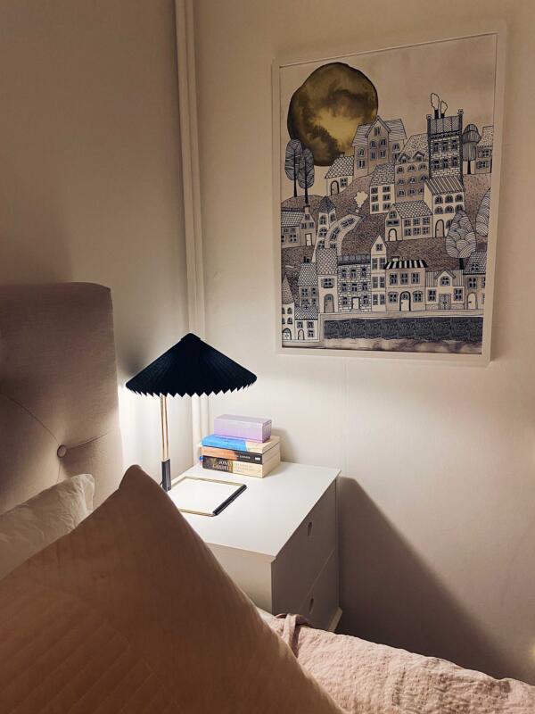 Tavla på väggen i ett sovrum.  Tavlans motiv är en detaljerad stad vid vattnet i svartvitt med en gul måne som lyser i himlen.