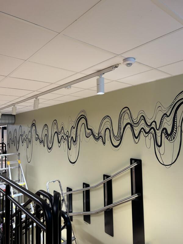 Väggmålning hos The Node i Stockholm i svart av vågiga linjer som föreställer ljudvågor och DNA