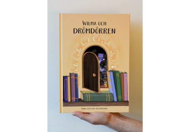 Framsida av omslaget till barnboken Wilma och Drömdörren som är gult med flera glada färger, en katt vinkar genom en öppen dörr