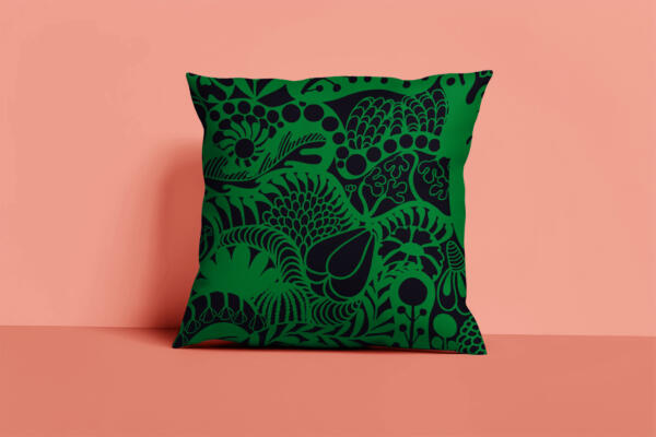 Kudde i svart och grönt med ett grafiskt och blommigt mönster. Rostig rosa bakgrund. Produktbild. Mönstret heter Lush.