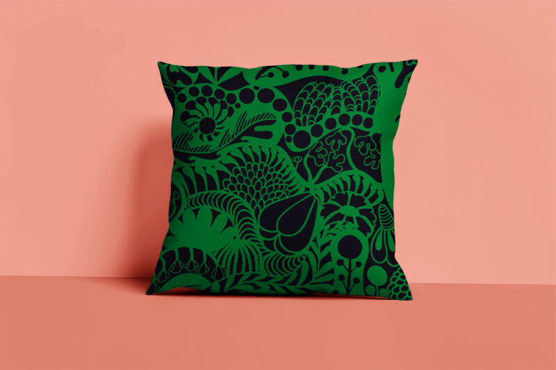 Kudde i svart och grönt med ett grafiskt och blommigt mönster. Rostig rosa bakgrund. Produktbild. Mönstret heter Lush.