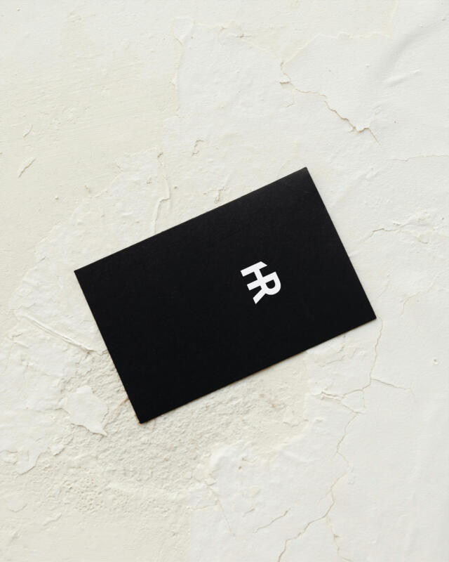 Svart visitkort med Heike Rüthers logo symbol på sandfärgad bakgrund