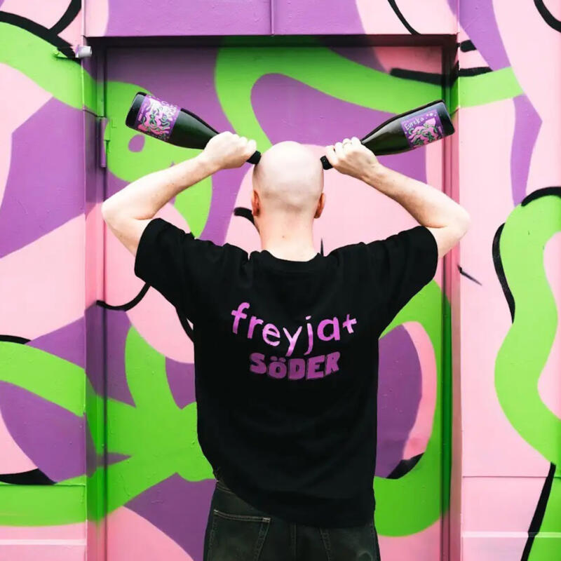 Ett foto av en man står med två flaskor mot en färgglad bakgrund av illustrationen till Freyjas egen cava