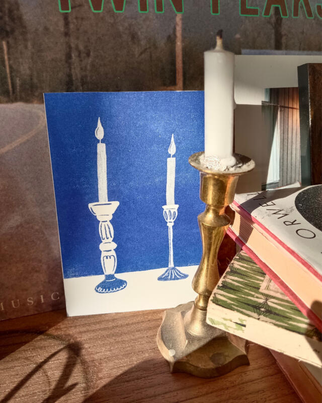 Vykort med två ljus i interiör med böcker och skivomslag i bakgrunden