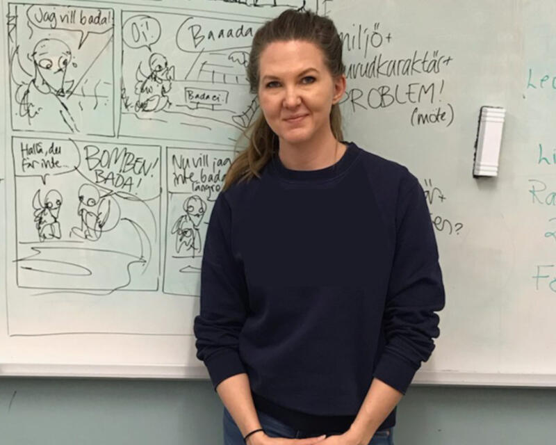 Yvette at a workshop, standing in front of a whiteboard with a sketched comic on it.