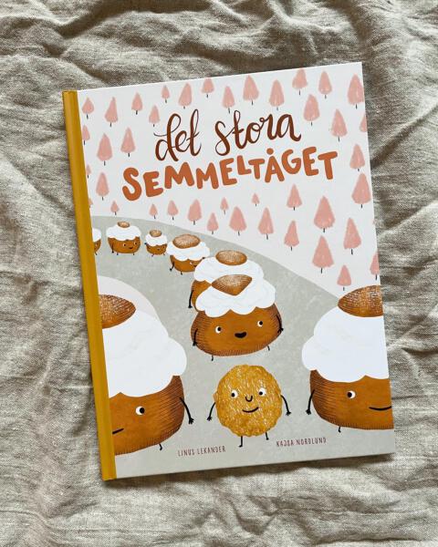 Omslagsbild av barnboken Det stora Semmeltåget. Illustrerade semlor står i led.
