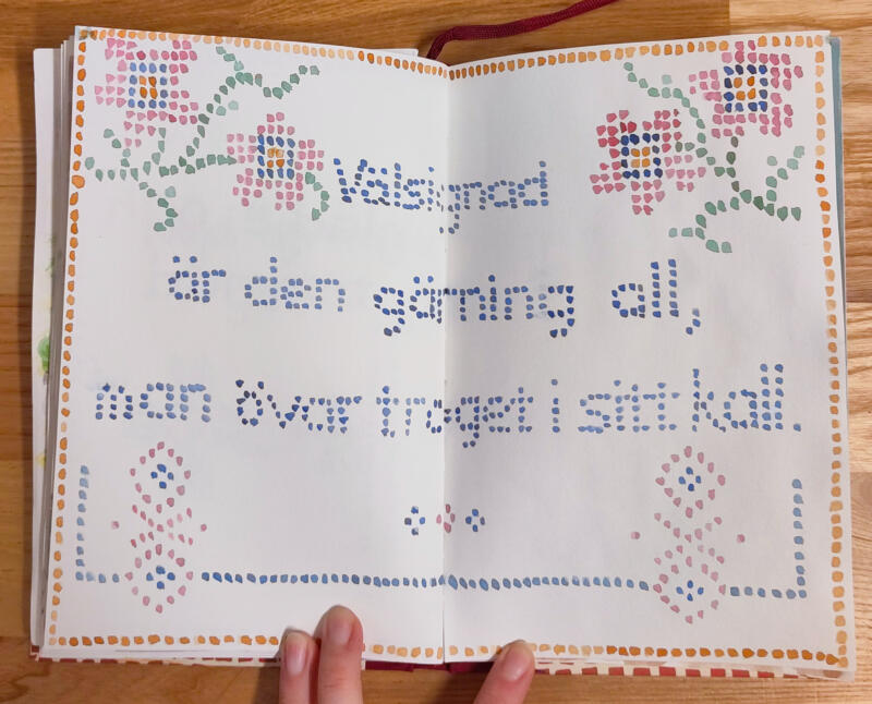 Akvarellmålning föreställande gammal väggbonad med korsstygn som bildar texten "Välsignad är en gärning all, man övar troget i sitt kall." och dekorativa blom-mönster