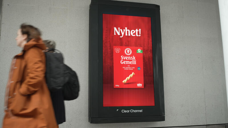 Film på en storbildsskärm på stan där reklamen om pastan visas. Två personer går förbi skylten.