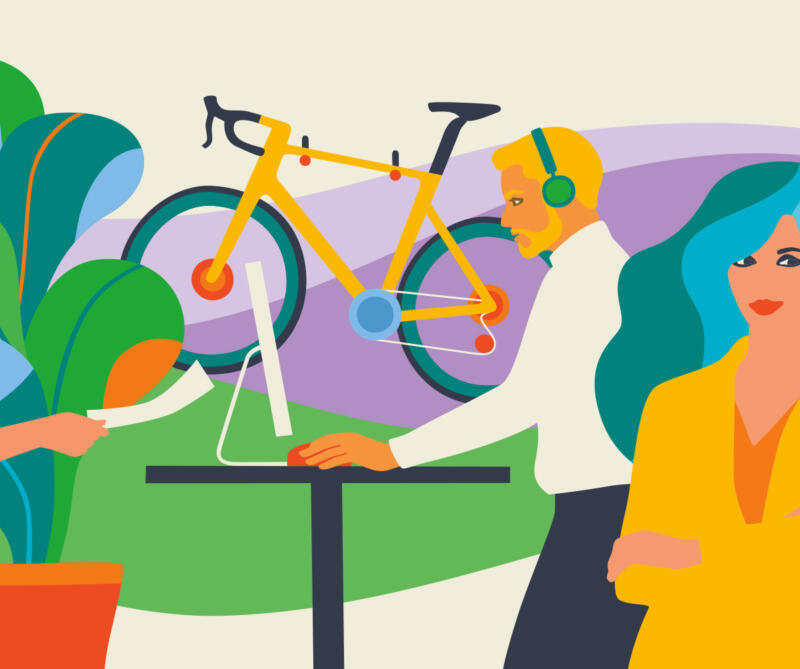 Skäggig man vid arbetsbord i kontorsmiljö med cykel och grön växt. Kvinna i kostym på samma arbetsplats.