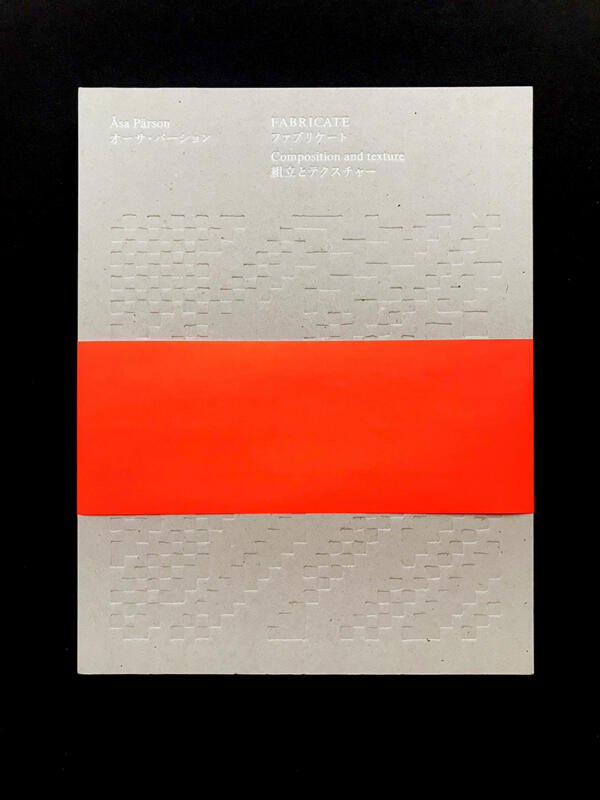 Omslagsbild av boken FABRICATE av textilformgivare Åsa Pärson. Omslaget har en blindpräglad illustration av rutigt vävrecept. Typografin är folierad i vitt. Boken är även skriven på japanska. Runt. boken finns en knallorange fluorescerande gördel i papper. Bokryggen är bunden med öppen rygg.