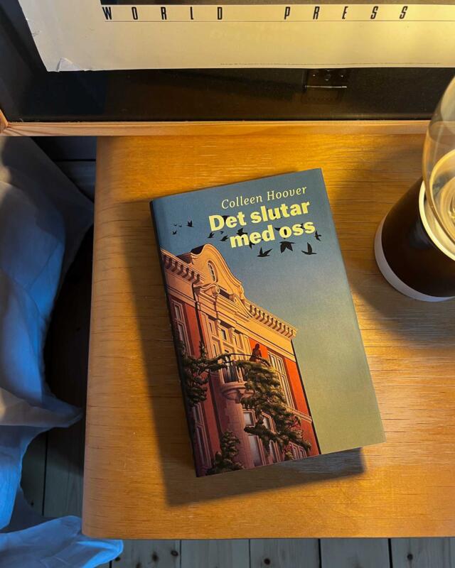 Bok som ligger på en nattduksbord. På bokens omslag fins en illustration av en byggnad med en balkong. På balkongen står en kvinna och tittar ut. På himlen flyger svarta fåglar. På byggnadens väggar klättrar väster med vita blommor. 