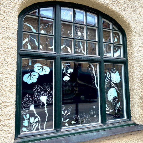 Foto på fönster med vita blommiga illustrationer.