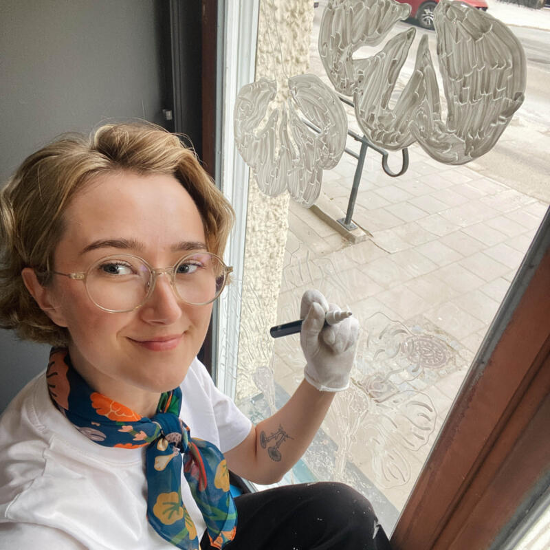 En bild på mig, Fia-Maria, som målat fönstret. I min vänstra hand håller jag en penna. 