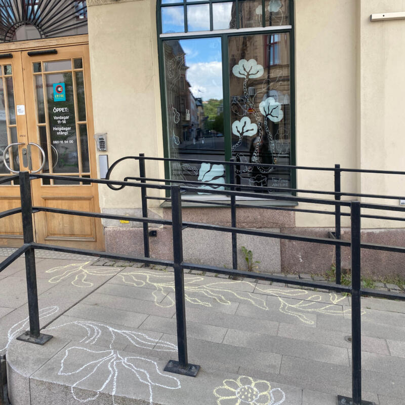 Blommor på trottoaren samt på fönstren. Illustrerade med vit färg.