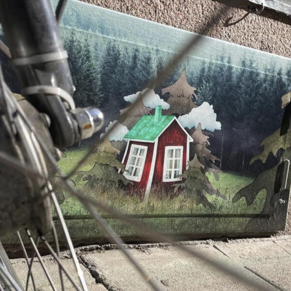 En illustration av en röd stuga med grönt plåttak omgiven av illustrerade granar och moln, omgiven av fotograferad mörk skog.