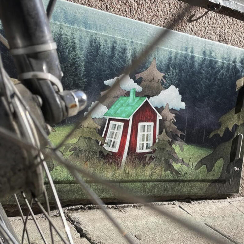 En illustration av en röd stuga med grönt plåttak omgiven av illustrerade granar och moln, omgiven av fotograferad mörk skog.