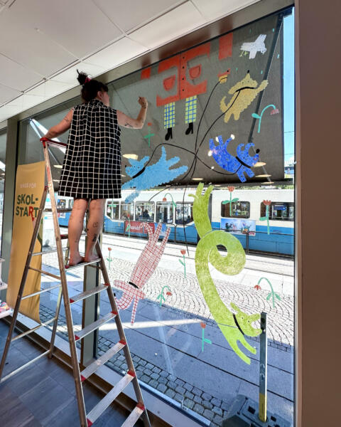 Moa Märta står på stege och målar på fönstret.