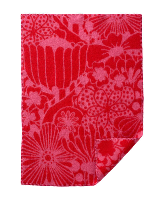 Barnfilt i rött och rosa med tråcklade kanter och nedre hörnet uppvikt. Ett blommigt mönster där påhittade blommor trängs. Prickar, ränder, streck, tentakler och klöver. En tolkning av urban växtlighet. Mönster utformat för att passa en barnfilt med mycket att titta på.