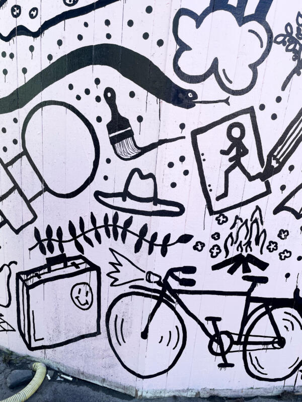 Väggmålning / muralmålning på del av ett byggplank vid Korsvägen i Göteborg. Rosa bakgrund med många svarta illustrationer, eller doodles, i olika storlekar. Detaljbild av en liten del av väggen.