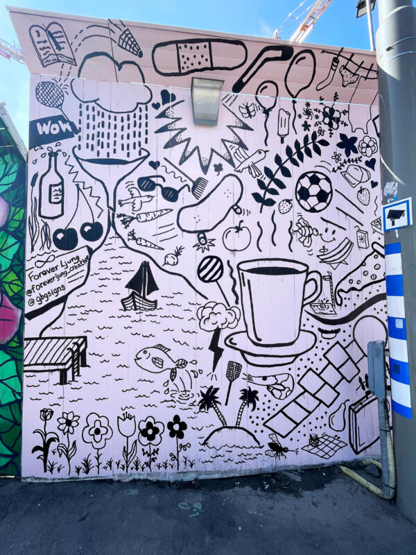 Väggmålning / muralmålning på del av ett byggplank vid Korsvägen i Göteborg. Rosa bakgrund med många svarta illustrationer, eller doodles, i olika storlekar. 