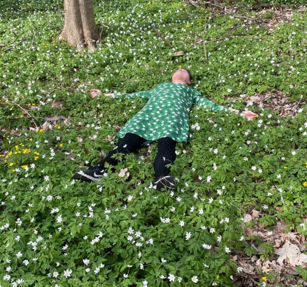 Kvinna ligger på marken bland vitsippor i en klänning med mönster av vitsippor.