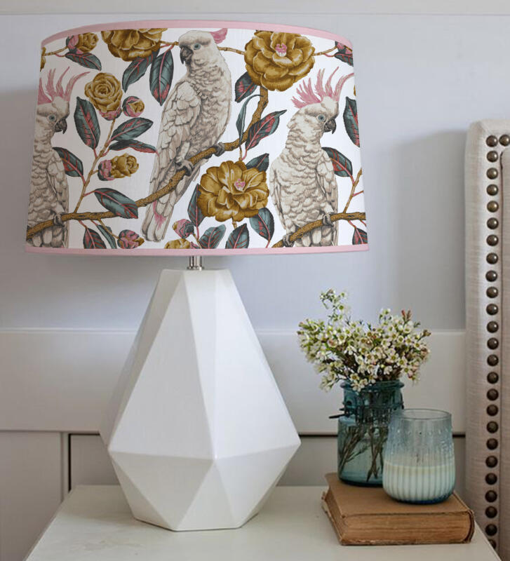 En lampa med handtecknat mönster på lampskärmen.  Mönstret föreställer ett par kakaduor omgivna av kameliablommor och blad i softa färger i rosa, turkos, senap och grågrönt. Ett harmoniskt och tilltalande mönster.