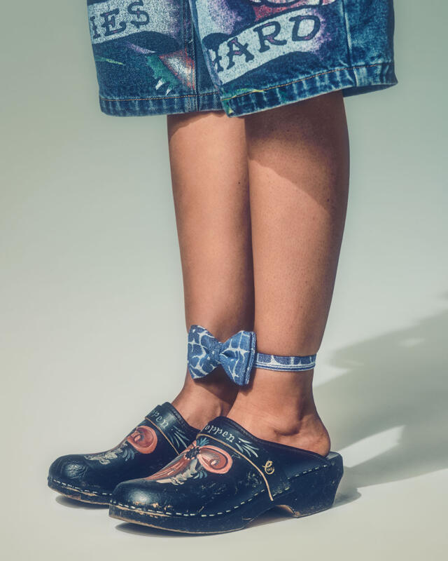 Tatuerade jeans shorts, bara ben, svarta träskor med almoge målning och en fluga runt anklarna.